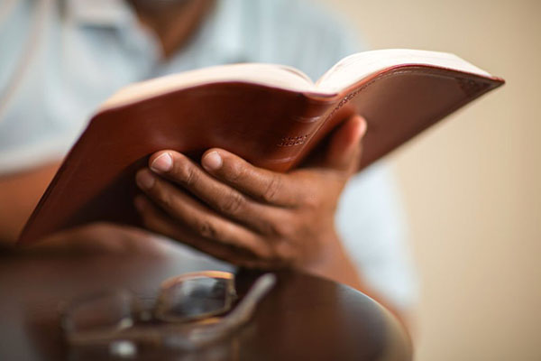 Mature African American man praying and reading the Bible.